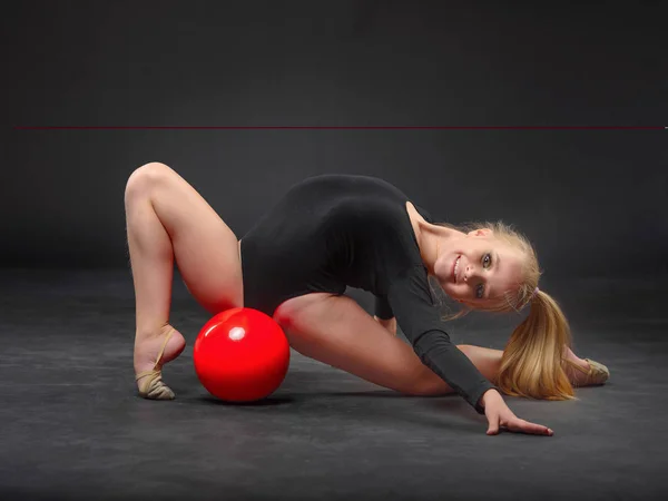 Joven hermosa blanca caucásica chica gimnasta haciendo ejercicio gimnástico con una pelota deportiva roja sobre fondo negro — Foto de Stock