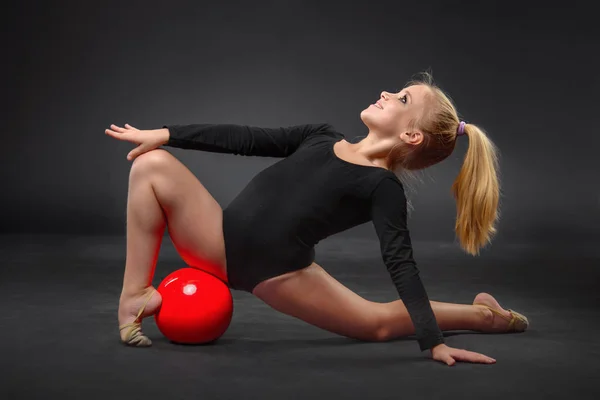 Joven hermosa blanca caucásica chica gimnasta haciendo ejercicio gimnástico con una pelota deportiva roja sobre fondo negro — Foto de Stock