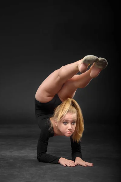 Young beautiful white caucasian girl gymnast with long hair doing gymnastic exercise on black background. — Stock Photo, Image