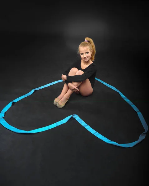 Young beautiful white caucasian girl gymnast resting on the floor with blue ribbon. Gymnastic tape in the form of heart