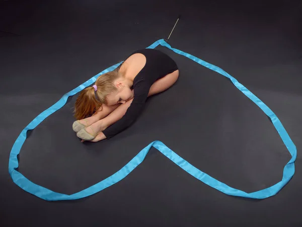 Young beautiful white caucasian girl gymnast resting on the floor with blue ribbon. Gymnastic tape in the form of heart