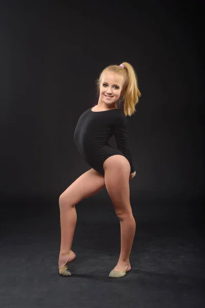 Молодая красивая белая кавказка гимнастка с длинными волосами делает гимнастические упражнения на черном фоне . — стоковое фото