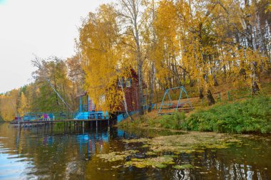 Eski ahşap ev güzel mavi bir gölün kıyısındaki sarı bir sonbahar ormanında yer almaktadır..