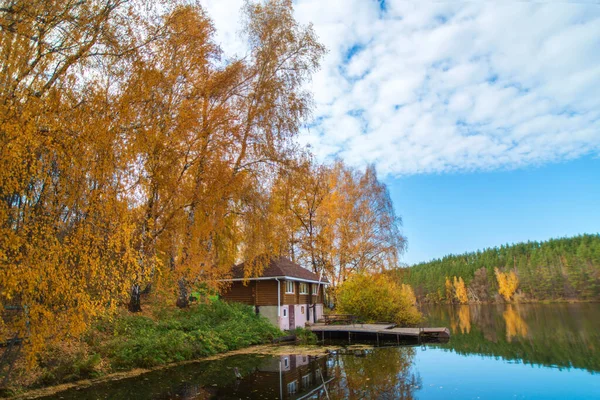 这所古老的木头房子坐落在美丽的蓝色湖畔的一个黄色的秋天的森林里 — 图库照片