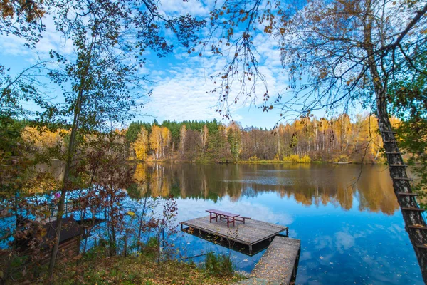 美丽的秋天风景 清澈的蓝湖 淡黄的秋天树 是的湖心有一个木制的小码头 上面有一张木制桌子和一条长椅 — 图库照片