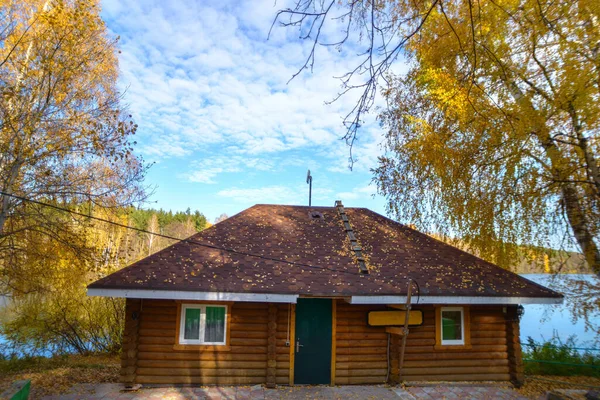 这所古老的木头房子坐落在美丽的蓝色湖畔的一个黄色的秋天的森林里 — 图库照片
