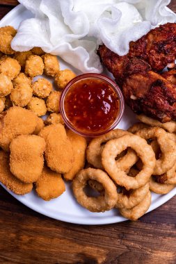 Beyaz tabakta bira için aperatifler servis edilmektedir: tavuk, tempura, soğan halkaları, tavuklu patlamış mısır ve biber sosu