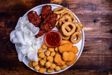 Beyaz tabakta bira için aperatifler servis edilmektedir: tavuk, tempura, soğan halkaları, tavuklu patlamış mısır ve biber sosu