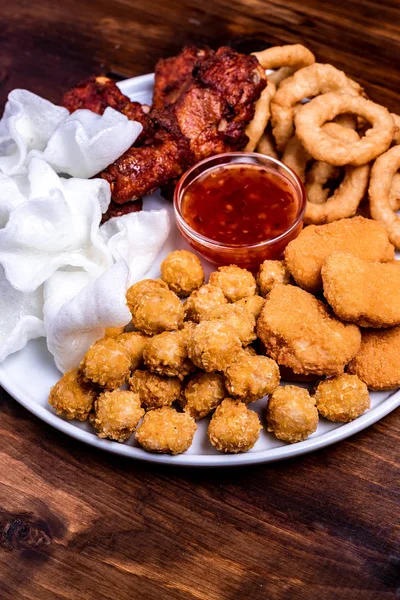 Snacks for beer on a white plate are: chicken nuggets, onion rings in tempura, chicken popcorn and chili sauce