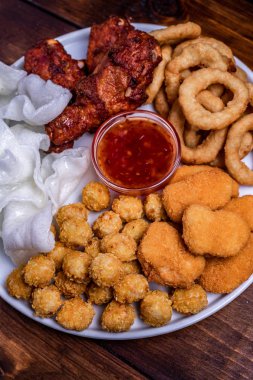 Beyaz tabakta bira için aperatifler servis edilmektedir: tavuk, tempura, soğan halkaları, tavuklu patlamış mısır ve biber sosu