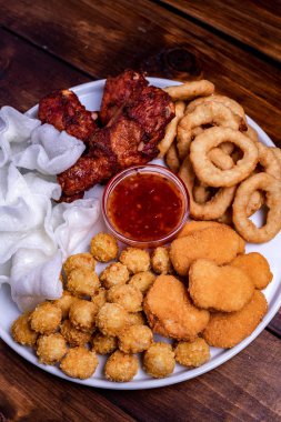 Beyaz tabakta bira için aperatifler servis edilmektedir: tavuk, tempura, soğan halkaları, tavuklu patlamış mısır ve biber sosu