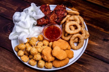 Beyaz tabakta bira için aperatifler servis edilmektedir: tavuk, tempura, soğan halkaları, tavuklu patlamış mısır ve biber sosu