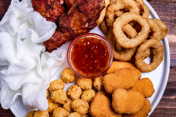 Beyaz tabakta bira için aperatifler servis edilmektedir: tavuk, tempura, soğan halkaları, tavuklu patlamış mısır ve biber sosu