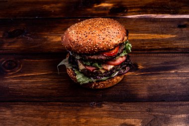 Koyu bir zemin üzerinde marul, peynir, soğan ve domatesli lezzetli ev yapımı hamburgerin yakın çekimi.