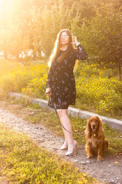 Atraktivní brunetka mladá žena s roztomilé štěně, procházka v parku, zelený trávník, olistění pozadí. — Stock fotografie