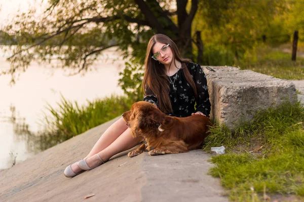 Mladá žena seděla se svým psem těší západ slunce — Stock fotografie