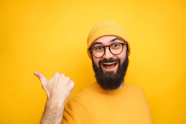 Colorful trendy man pointing away on yellow