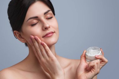 Genç bir kadın yüzüne krem sürüyor.