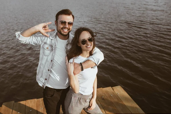 Feliz pareja en el muelle mostrando los cuernos gesto —  Fotos de Stock