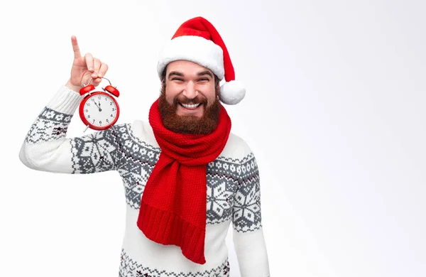 Homem barbudo segura um relógio vermelho e sorri sobre fundo branco . — Fotografia de Stock