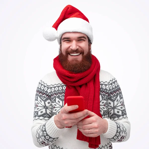 Homem com barba segura celular e sorri no Natal — Fotografia de Stock