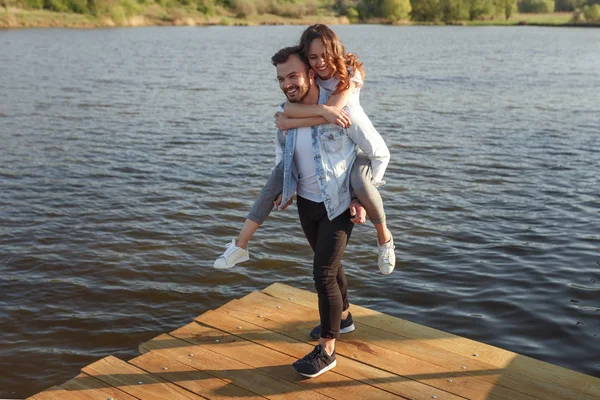 Man carrying girlfriend piggyback on pier — Stock Photo, Image