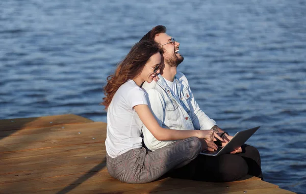 Lyckliga par med laptop kylning på piren — Stockfoto