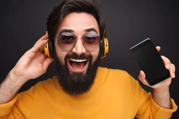 Chico alegre en auriculares que muestran el teléfono inteligente —  Fotos de Stock