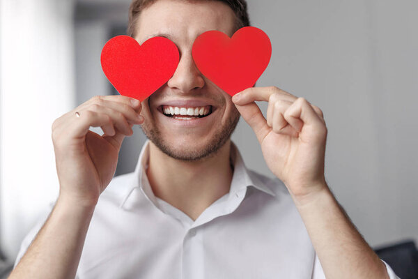 Cheerful guy holding hearts near face