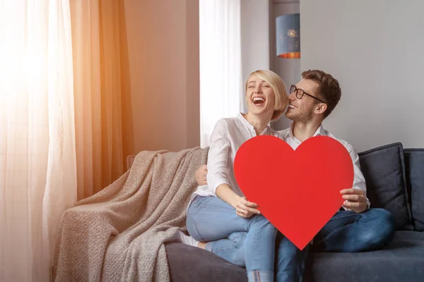 Laughing couple with heart on sofa — Stock Photo, Image