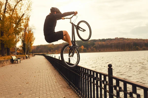 Anonymous man on bike doing tricks on embankment — Stock Photo, Image