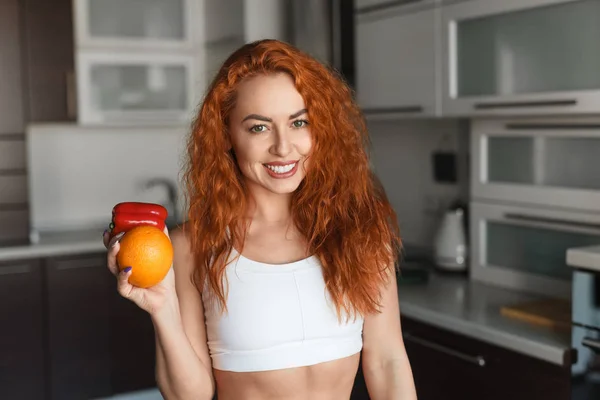 Senhora sorridente com laranja e pimenta na cozinha — Fotografia de Stock