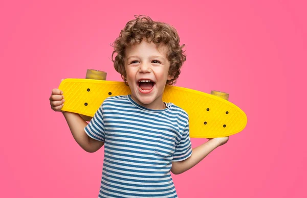 Щасливий кучерявий хлопчик сміється і тримає скейтборд — стокове фото