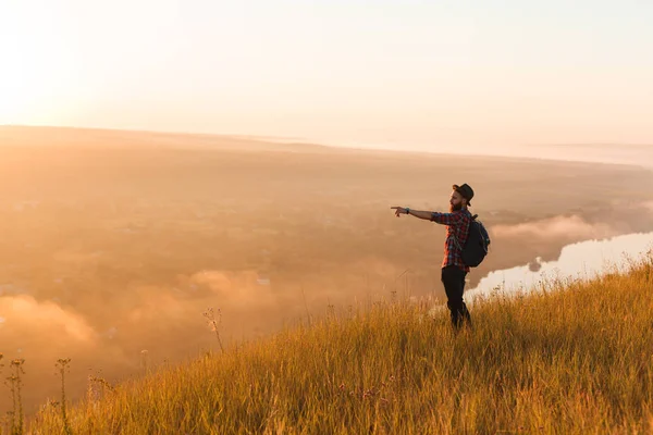 Traveling hipster pointing away in nature — Stock Photo, Image