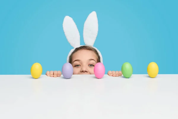 Chica con asomarse por detrás de la mesa con huevos de Pascua — Foto de Stock