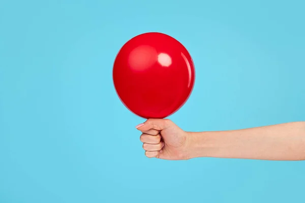 Mano sosteniendo globo rojo sobre fondo azul — Foto de Stock