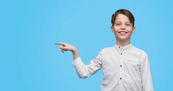 Glimlachend jongen weg wijzen op blauwe achtergrond — Stockfoto