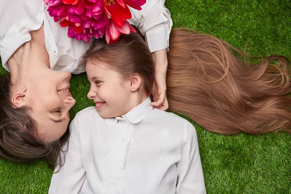 แม่กับช่อดอกไม้นอนใกล้ลูกสาวบนหญ้า — ภาพถ่ายสต็อก