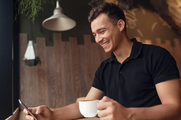 Wesoły facet z kawy przeglądania smartfonem w kawiarni — Zdjęcie stockowe