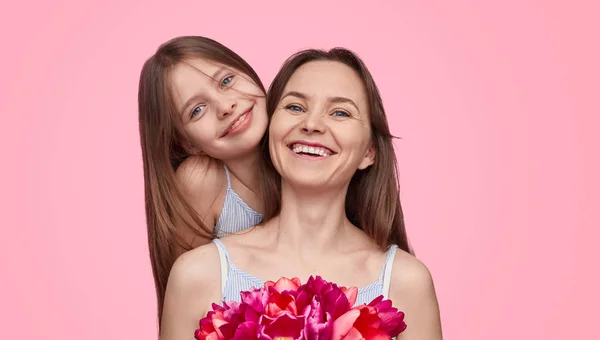 Cheerful mother and daughter with bouquet looking at camera — Stock Photo, Image