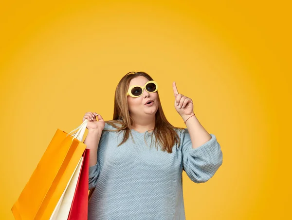 Sorprendida hembra regordeta con bolsas de papel apuntando hacia arriba —  Fotos de Stock