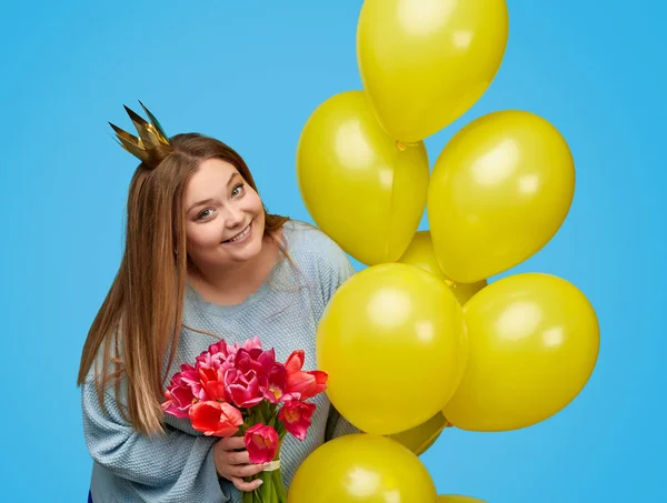 Plump lady with flowers and balloons looking at camera