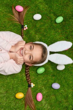 Heyecanlı kız Paskalya yumurtaları yakınındaki çim üzerinde yalan