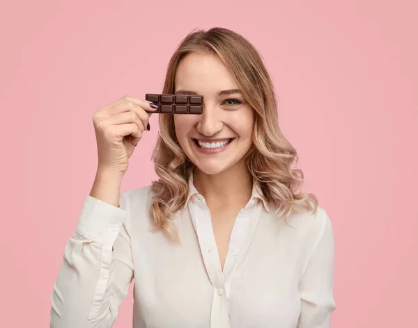 Veselá žena drží čokoládový poblíž oko — Stock fotografie
