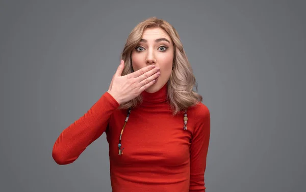 Woman in sweater covering mouth in astonishment