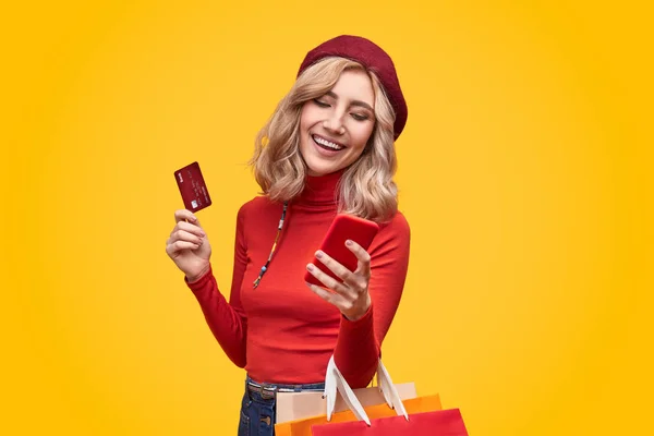 Женщина с пластиковой картой и бумажными пакетами с помощью смартфона — стоковое фото
