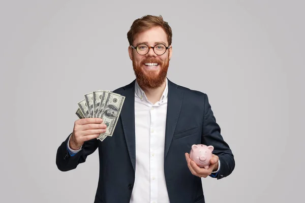 Hombre de negocios alegre con dinero en efectivo y alcancía —  Fotos de Stock