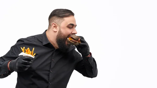 Homem com batatas fritas mordendo hambúrguer — Fotografia de Stock