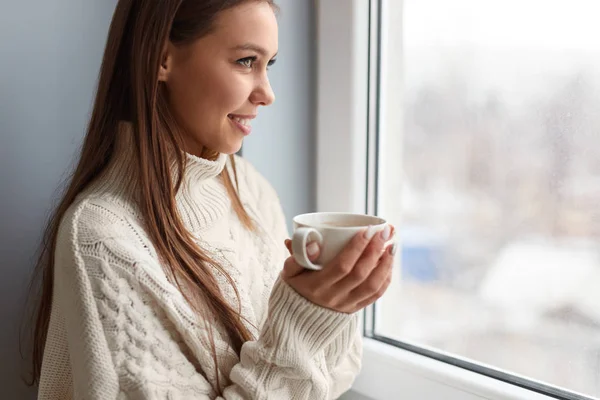 Mujer sonriente con café caliente cerca de la ventana — Foto de Stock