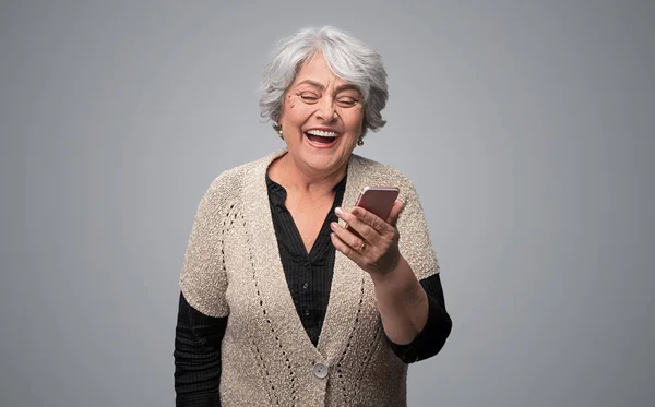 Смеющаяся пожилая женщина просматривает смартфон — стоковое фото